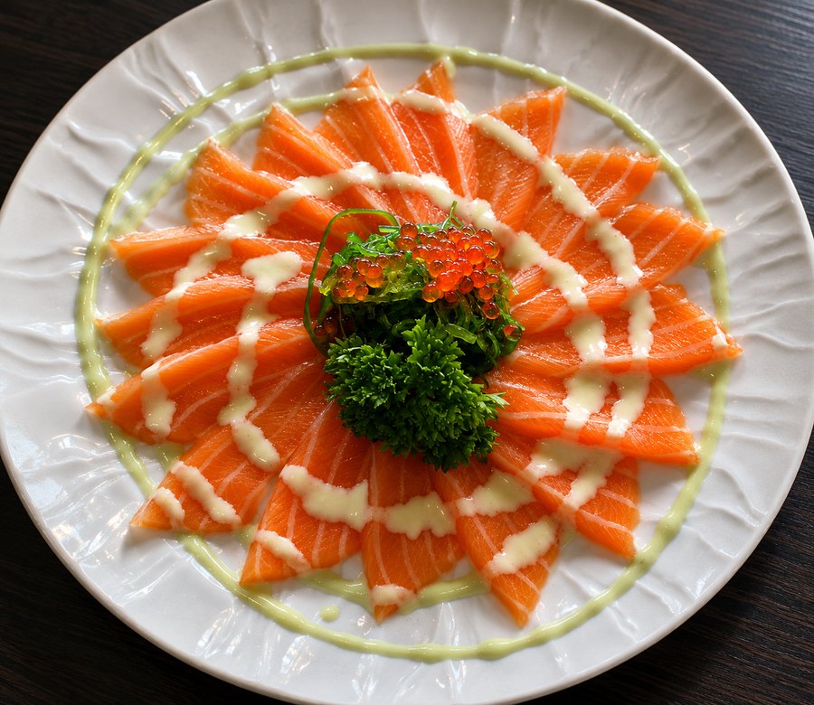 Laksesashimi i vifte på hvitt fat, med rogn og persille i midten.