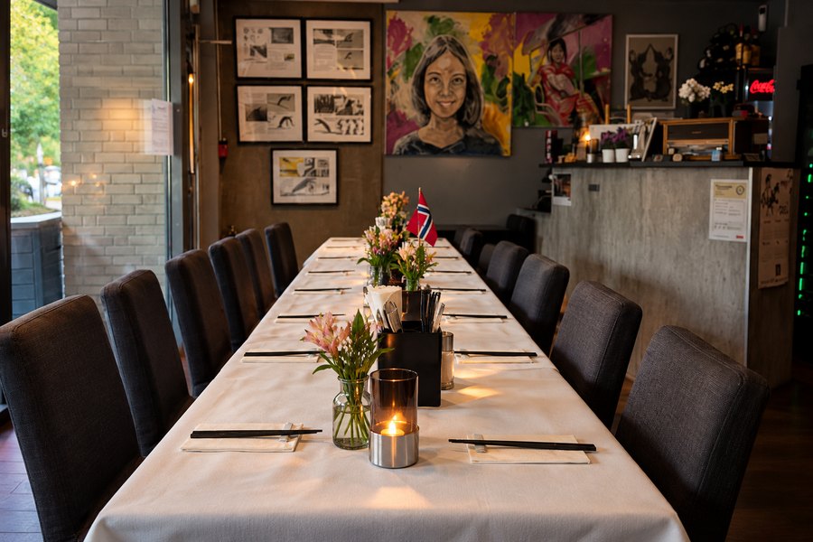 Langbord dekket med hvit duk, blomster og levende lys i restauranten.